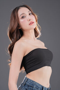 Beautiful Asian woman with glowing skin and brown hair, professional beauty portrait of young female in black tube top on grey background