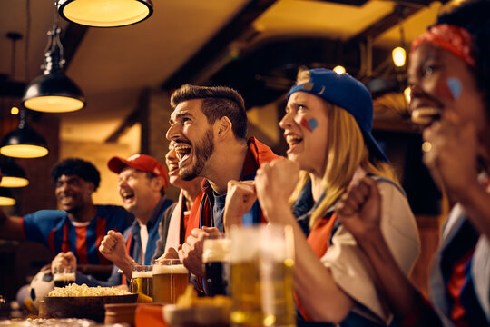 Excited supporters cheering for their winning team while watching live sports event in pub.