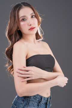 Beautiful Asian woman with healthy skin and long wavy hair smiling, glowing skin and beauty portrait of young female on grey background