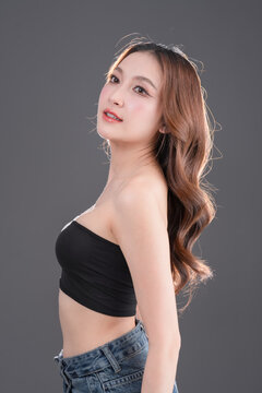 Beautiful Asian woman with healthy skin and long wavy hair smiling, glowing skin and beauty portrait of young female on grey background