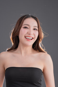 Beautiful Asian woman with healthy skin and long wavy hair smiling, glowing skin and beauty portrait of young female on grey background