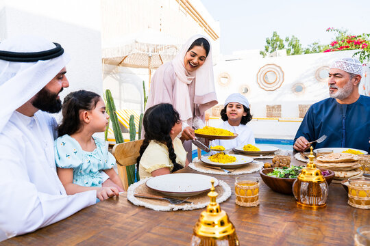 Arab family wearing traditional emirati clothing having lunch at home in the backyard garden - Middle-eastern family bonding and having fun on a family reunion dinner