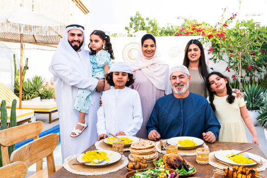 Arab family wearing traditional emirati clothing having lunch at home in the backyard garden - Middle-eastern family bonding and having fun on a family reunion dinner