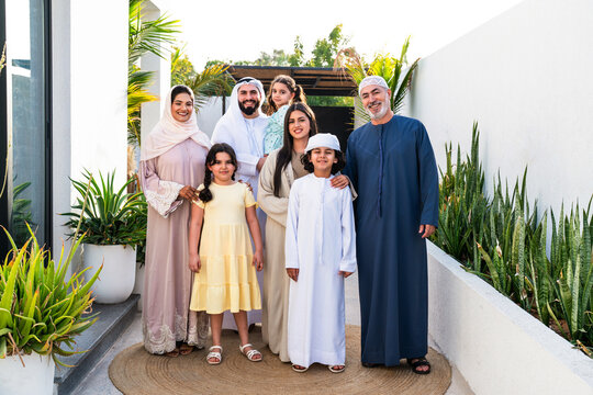 Arab multigenerational family wearing traditional emirati clothing standing together in modern home garden in Dubai