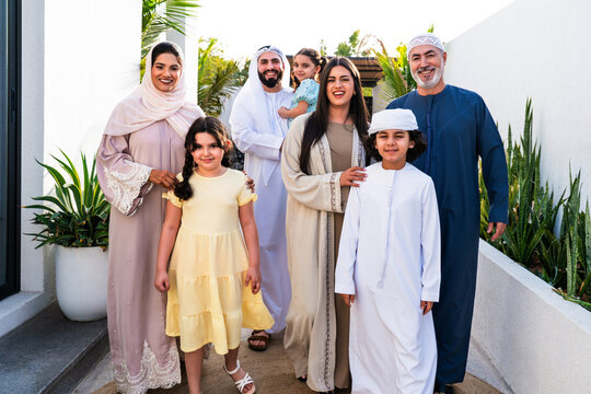 Arab multigenerational family wearing traditional emirati clothing standing together in modern home garden in Dubai