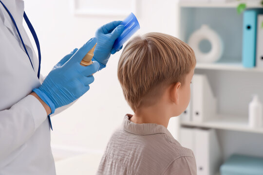 Female doctor with remedy brushing little boy's hair with pediculosis in clinic, closeup