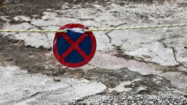 Closeup of a red blue no stopping traffic sign blocking walkway swaying on the wind. 
