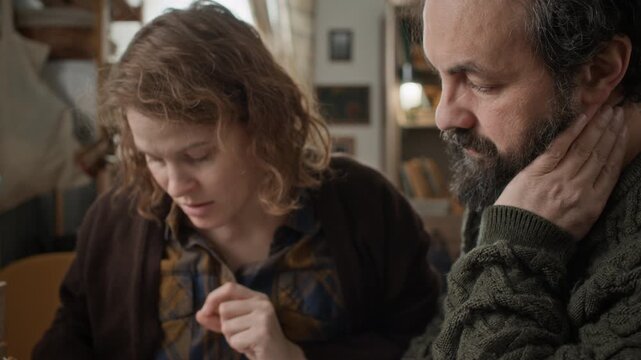 Low angle tilt up shot of poor couple of middle aged man and woman calculating past due bills in rundown apartment