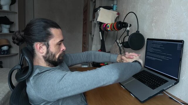 Recognizable Caucasian Young Man with Bun Hair Typing on Laptop then Stretching Arms Upwards and Leaning Back with Hands Behind Head to Rest in Home Office Eye Level Side View Profile Day Shot