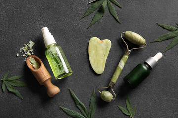 Obraz premium Bottles of hemp cosmetic products with sea salt, facial massage tools and leaves on black background