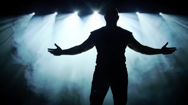 A powerful silhouetted male figure on a vast black stage with outstretched arms, pierced by cinematic spotlights, god rays through thick smoke, low angle crane video, profound majesty concept.