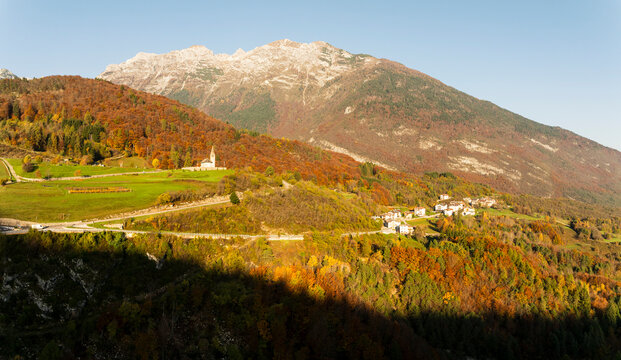 Autumn landscape with San Tommaso church, a charming village, and vibrant forests nestled in a scenic mountain valley, ideal for tourism and outdoor travel in Cavedago, Paganella, Trentino, Italy.