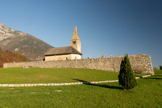 San Tommaso church, historical landmark, on a green hill with a stone wall, backed by autumn mountains offers a serene tourism destination with copy space in Paganella, Trentino, Italy.