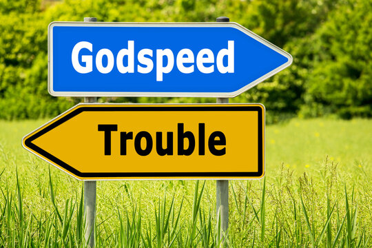Signpost shows directions with words Godspeed and Trouble on a sunny day in a grassy area