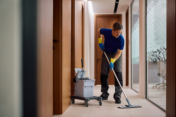 Commercial cleaner using mop while cleaning office hallway.