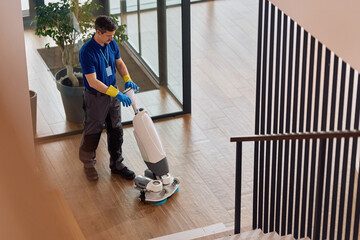 Janitor using professional floor scrubbing machine while cleaning corporate office lobby.