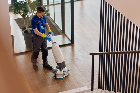 Janitor using professional floor scrubbing machine while cleaning corporate office lobby.
