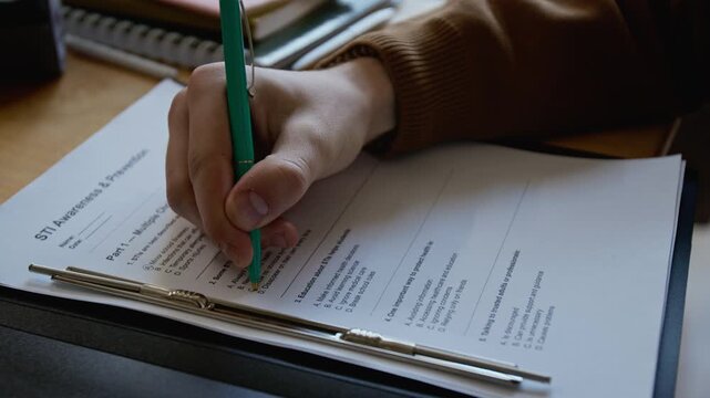 Close-up of hand of anonymous male student writing STI awareness test at reproductive health course, choosing correct answers to questions on methods of infection prevention and protection