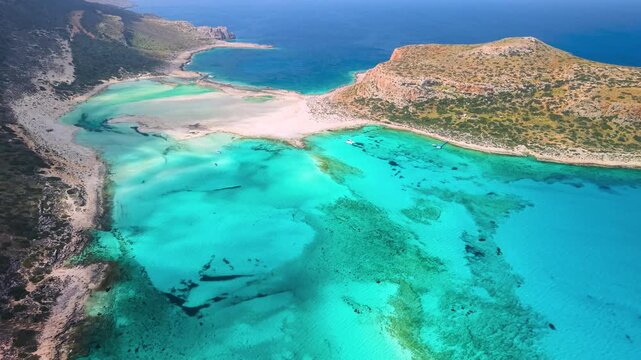 Aerial view of Balos lagoon with turquoise Caribbean-like water and luxury catamaran yacht. Sandy beach at Gramvousa island with ochre cliffs and deep blue sea. Exotic summer mood in Crete 4k.