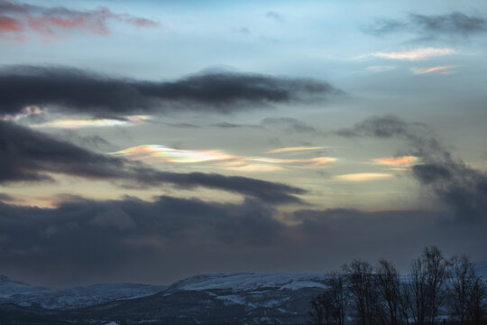 Rare iridescent nacreous cloud glowing in a pastel Arctic twilight sky above dark clouds, soft atmospheric winter scene in Norway