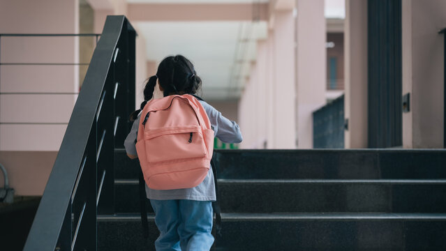Young student with pink backpack climbing stairs in school hallway, promoting education, growth, and determination in children's daily life journey