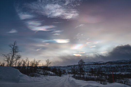 Rare iridescent nacreous cloud glowing in a pastel Arctic twilight sky above dark clouds, soft atmospheric winter scene in Norway