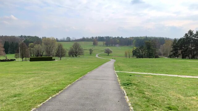 Walking path leading through open green landscape in Lidice under soft cloudy sky. Peaceful location in the Czech Republic with gentle scenery and quiet atmosphere of reflection.