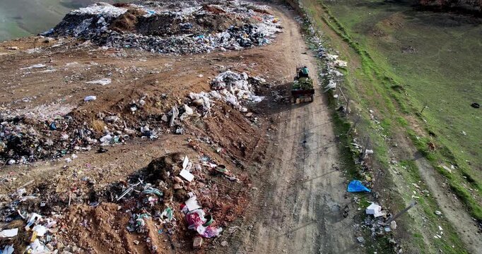 Tractor with a trailer transporting garbage for dumpig on open landfill, aerial view