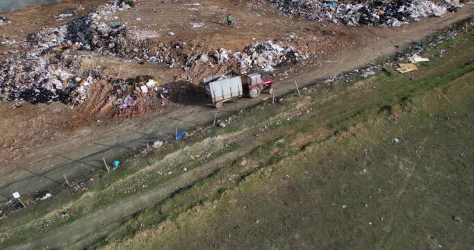 Tractor with a trailer transporting garbage for dumpig on open landfill, aerial view