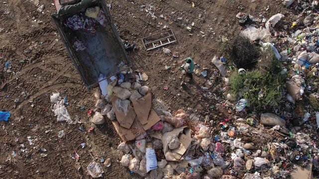 Garbage transportation by tractor pulling a trailer on rural road. Landfill dumping illegal activity, aerial view