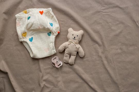 White cotton baby diaper pantie and toys on beige sheet, top view. Eco friendly cloth