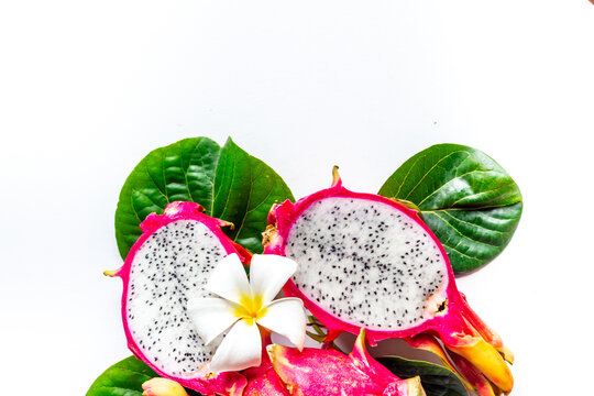 Yummy pitahaya dragon fruits with frangipani flower and green leaves on white table. Tropical fruits food, top view