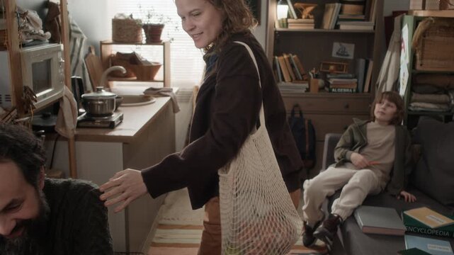 Tilt up shot of woman returning with groceries to her husband and kids in a small, poor, rundown apartment