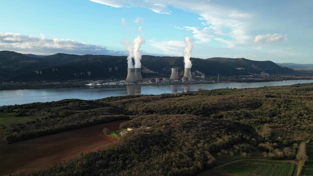Cruas, France - 20 February 2026: Aerial drone view of the Cruas nuclear power plant in France, with cooling towers producing steam beside the Rh&ocirc;ne River during a dramatic sunny afternoon landscape.