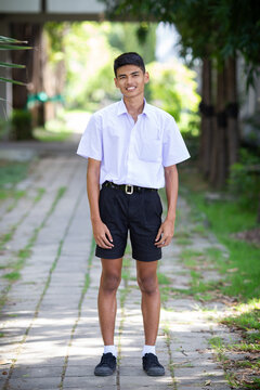 Thai boy student in official Thai school uniform (black shorts), ordinary appearance with slightly dark complexion, stand firmly on a walkway with arms at his sides, portrait orientation