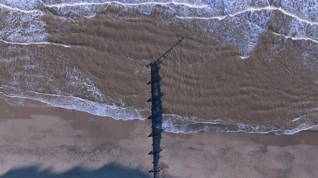A top down Birds Eye view of a wooden groyne in the sea as the tide is coming in