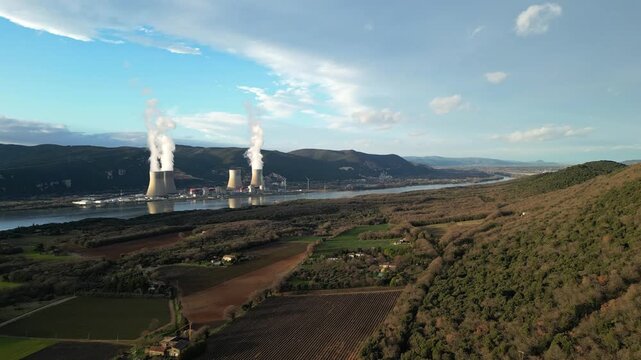 Cruas, France - 20 February 2026: Cinematic drone flyover above the Cruas nuclear power station in France, showing massive cooling towers with steam rising near the Rhone River and surrounding country