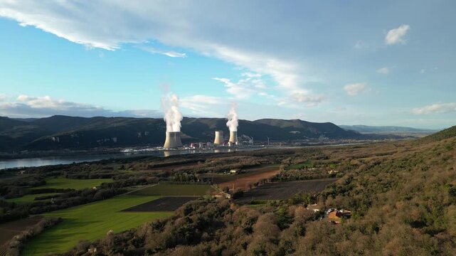 Cruas, France - 20 February 2026: Cinematic drone flyover above the Cruas nuclear power station in France, showing massive cooling towers with steam rising near the Rhone River and surrounding country