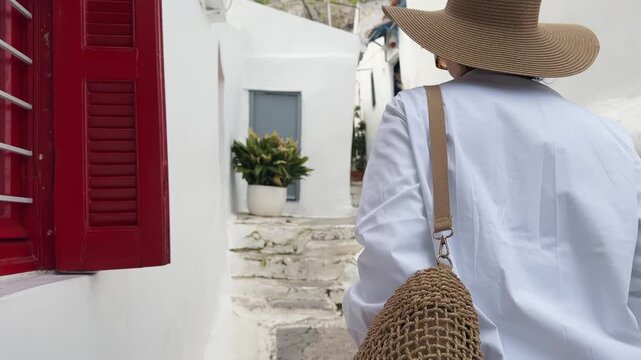 Portrait of a stylish young woman in a hat and a white shirt walking on old street in Anafiotika, Plaka in Athens, Greece
