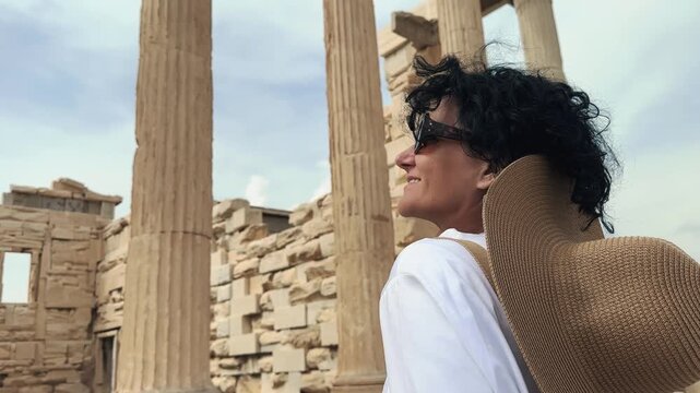 Hispanic curly hair fashion woman with hat is visiting Parthenon, Acropolis in ancient Athens, Greece