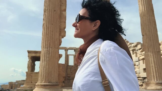 Young fashion woman visiting ancient Acropolis in Athens a Greek monument with stone columns, wearing white shirt, hat and stylish glasses