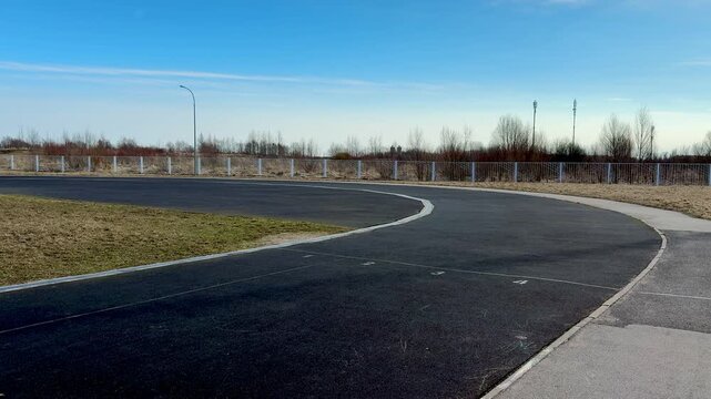 Close-up running track asphalt surface curve showing granular rubber texture, faded lane marking and grassy verge, empty prerace