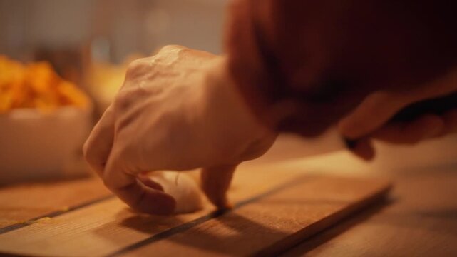 In warmly lit kitchen, a man's hands skillfully slice a freshly peeled onion bulb into thin rings, releasing aromatic flavors and showcasing culinary expertise with a fresh root vegetable preparation