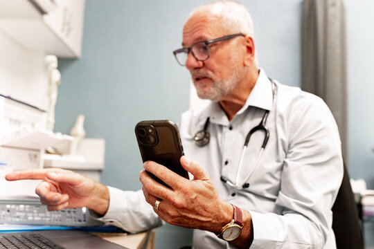 Doctor with stethoscope in virtual consultation using smartphone and laptop