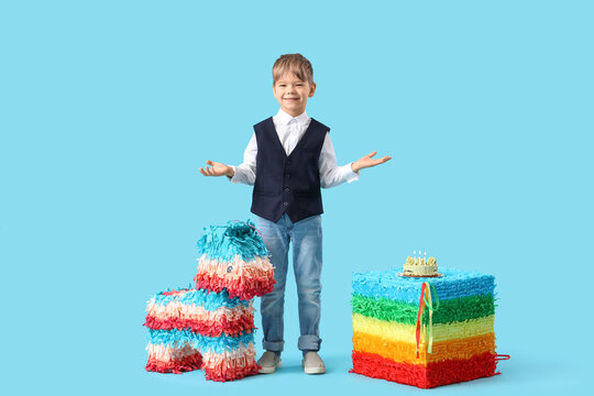Cute little boy with Birthday cake and pinatas on blue background