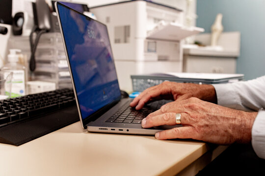 Married healthcare worker typing on laptop in clinical office