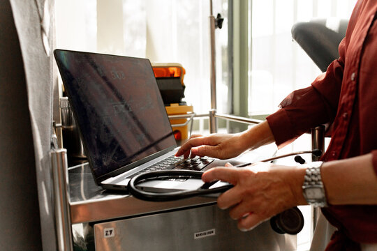 Healthcare professional working on laptop in clinic while holding a stethoscope