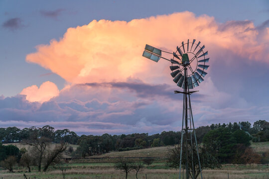 Farm windmill silhouetted against a pink thunderhead over rural farmland