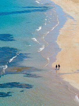 Distant aerial view of a couple walking through waves along a sandy beach