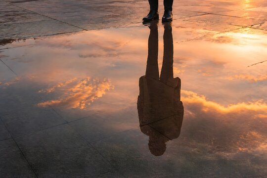 Reflection of a business person in water puddle at sunset, silhouette concept of identity and introspection